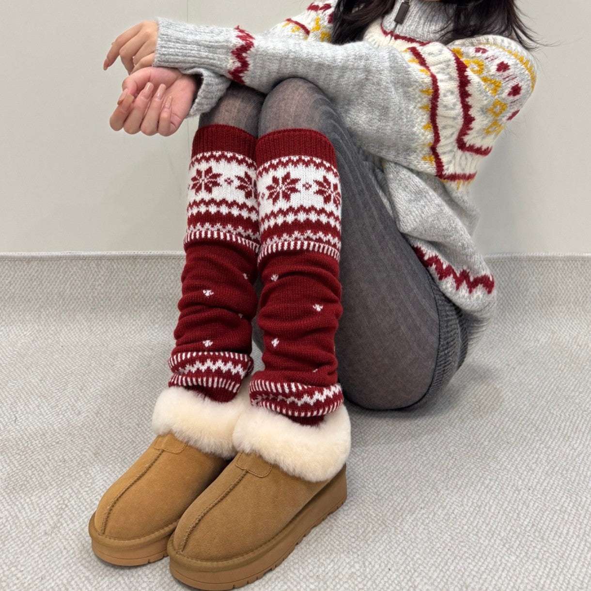 Women wearing red knitted thermal leg warmers with white snowflake pattern and brown fur-lined boots sitting on floor